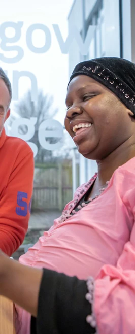 Lecturer in an orange hoodie and a student in a pink top smiling while working together on assembling a blue robotic vehicle near a large window with Glasgow Kelvin College branding Lecturer in an orange hoodie and a student in a pink top smiling while working together on assembling a blue robotic vehicle near a large window with Glasgow Kelvin College branding